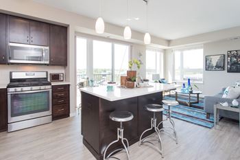 Open and contemporary kitchen with island and overhead pendant lighting. Stainless steel appliances are in view.